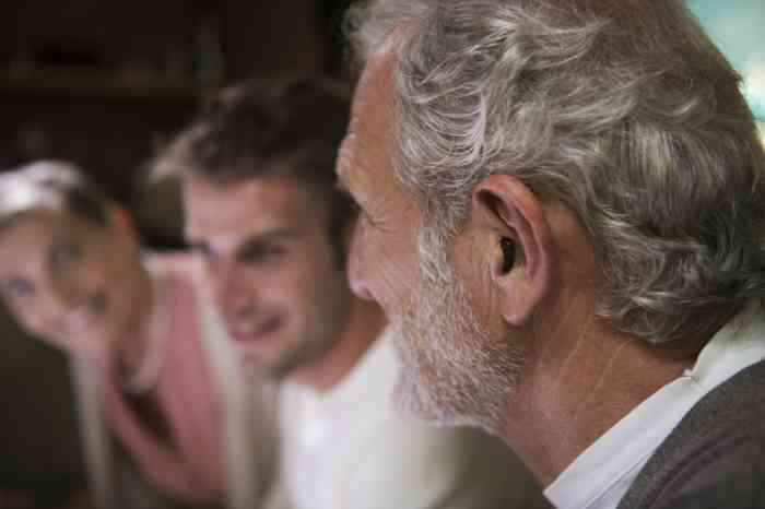 Homem com aparelho auditivo ampli-mini acompanhado da família durante um convívio