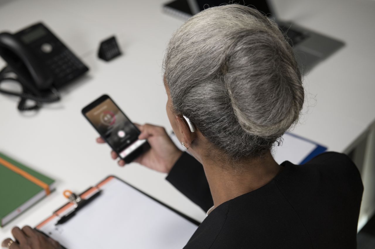 senhora com aparelhos auditivos e telemóvel na mão