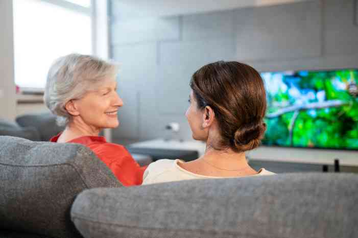 Senhora com aparelhs auditivos fala com a filha e ouve a televisão