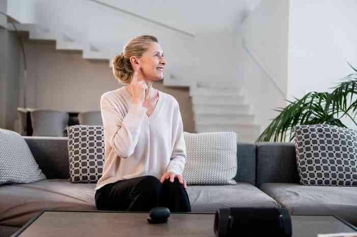 Mulher com aparelho auditivo sentada no sofá da sua casa, a ouvir todos os sons ao seu redor