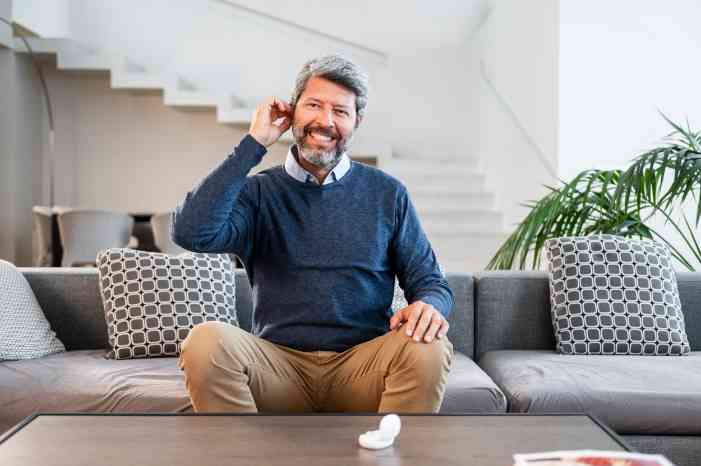 Cliente Minisom, na sala da sua casa, a colocar o aparelho auditivo no ouvido