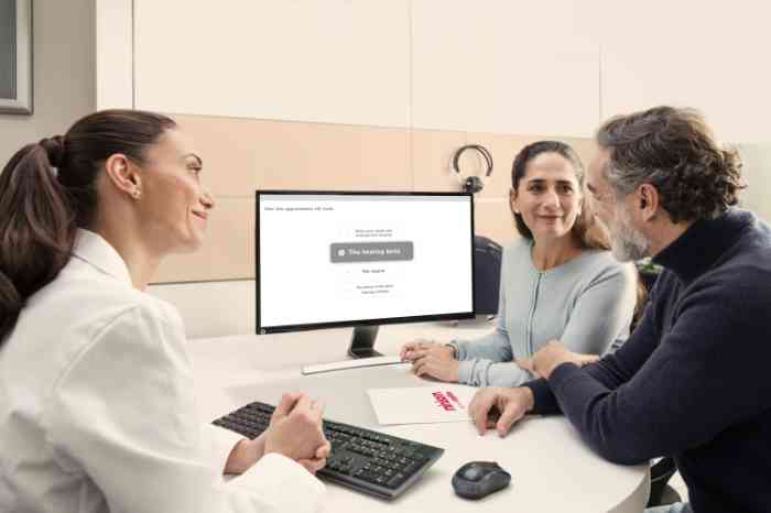 Audiologista no consultório com dois clientes, um homem e uma mulher.