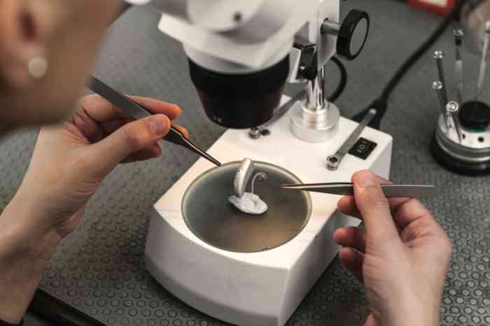 Audiogista observa aparelho auditivo com microscópio