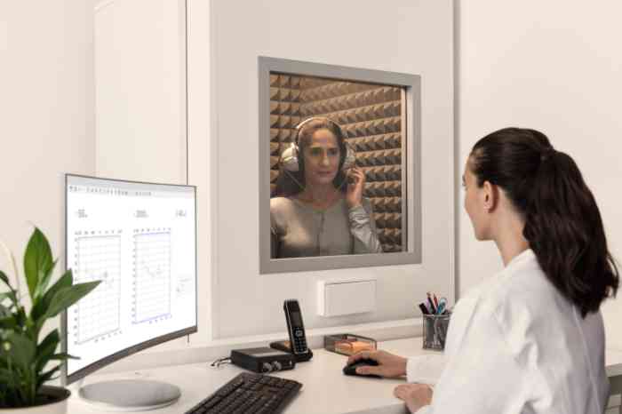 Audiologista faz exame auditivo a senhora que está no espaço insonorizado.