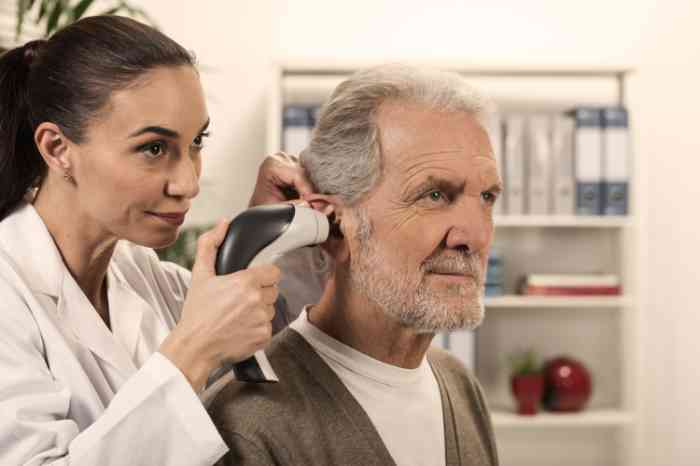 Audiologista com otoscopio a observar ouvido de homem