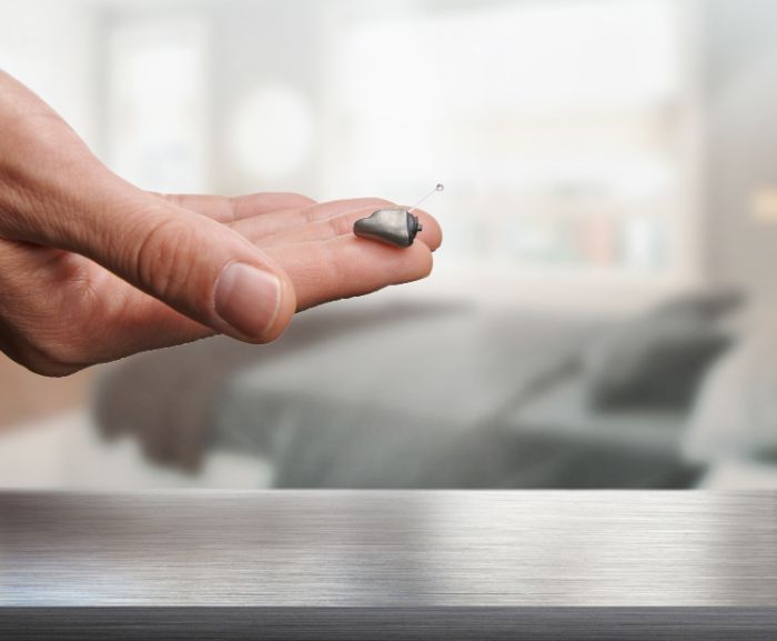 Pequeno aparelho auditivo ITE na mão.