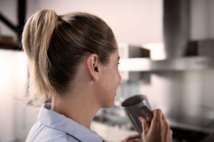 Senhora com aparelho auditivo dentro do ouvido toma o café.