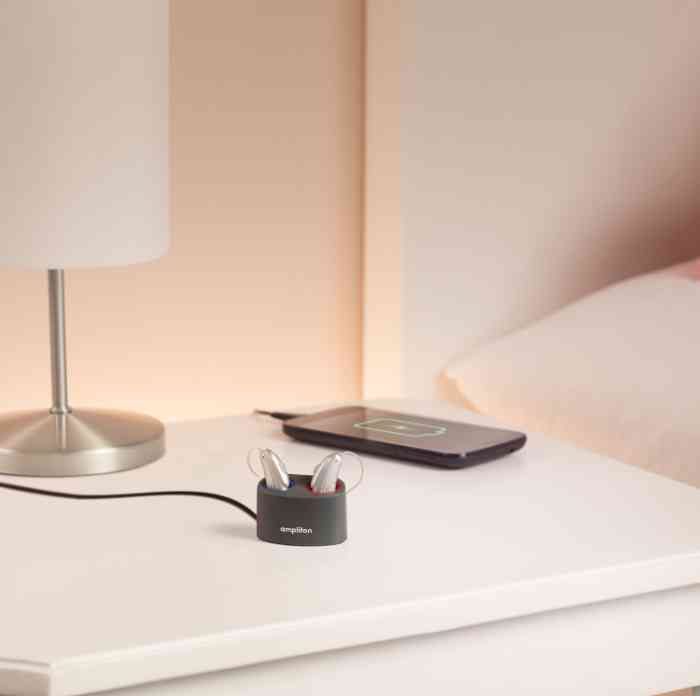 Aparelhos auditivos carregam bateria na mesa de cabeceira.