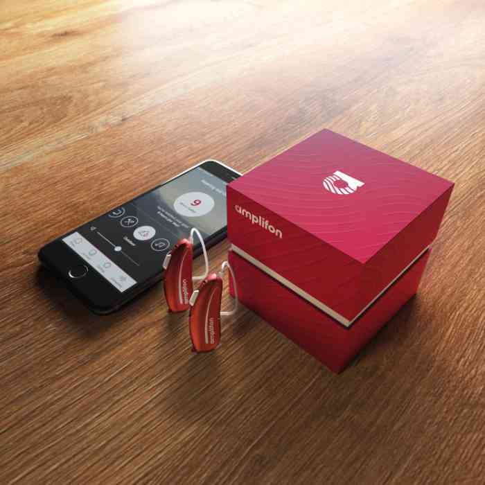 Telemóvel, aparelhos auditivos e caixa vermelha em forma de cubo em cima de uma mesa