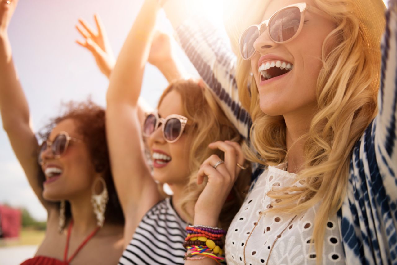 Jovens do sexo feminino num concerto musical, divertidas, a cantarem e com os braços no ar.