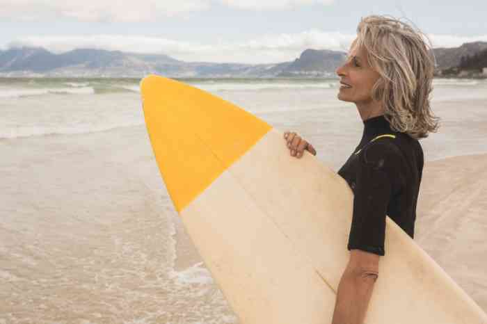 Senhora com prancha de surf na mão numa praia.