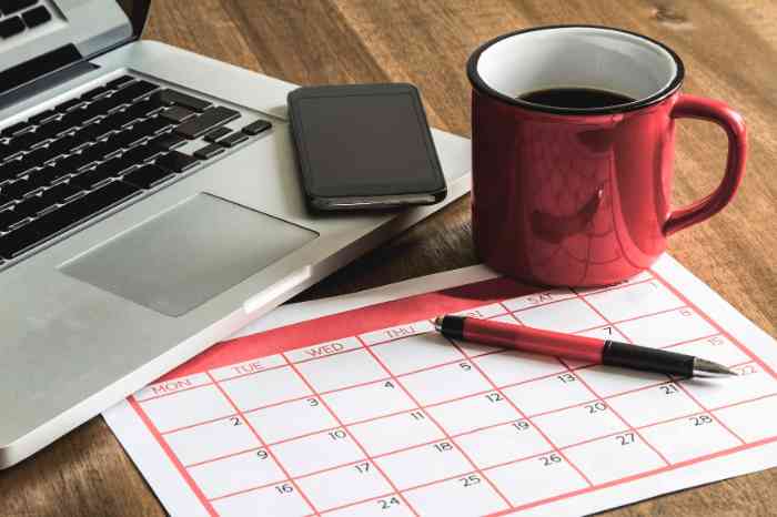 Secretária com uma caneca, um calendário, um telemóvel e um portátil
