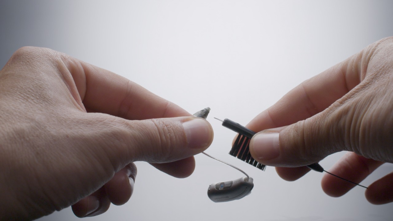 Aparelho auditivo RIC está a ser limpo com a escova de limpeza.