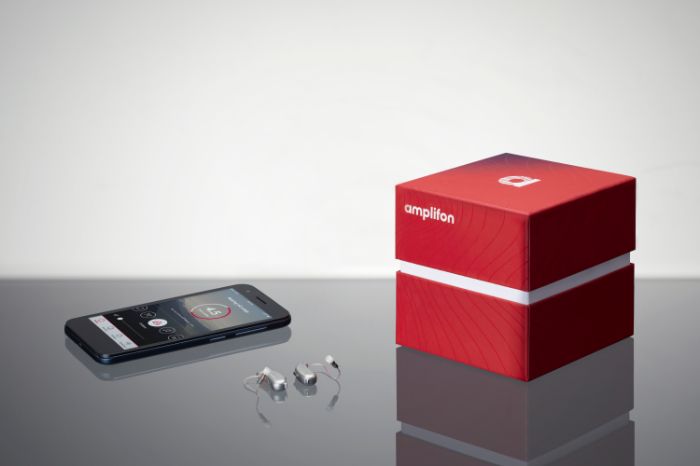 Cubo vermelho e caixa com aparelhos auditivos recaerregáveis e um telemóvel