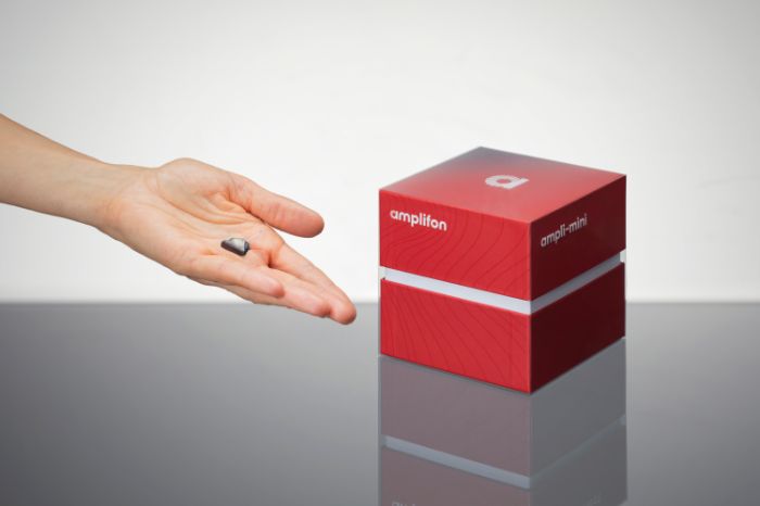 Mão com aparelhos auditivos e respetiva caixa em forma de cubo vermelho
