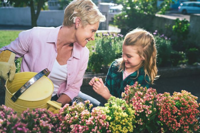Senhora de idade com implante osteointegrado encontra-se num jardim a cuidar das suas flores, acompanhada de uma criança.