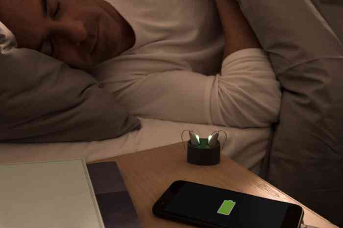 homem a dormir com aparelhos auditivos e telemóvel na mesa