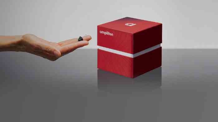 Mão com aparelhos auditivos e sua caixa vermelha em forma de cubo