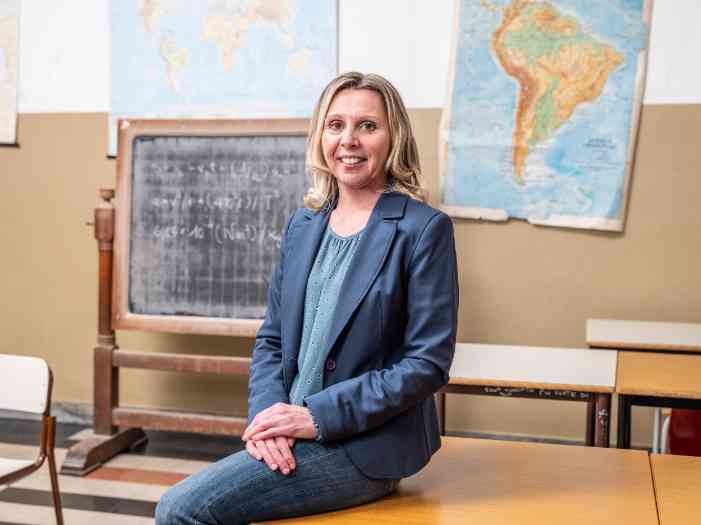 Professora a posar, sentada em cima de uma mesa, numa sala de aula