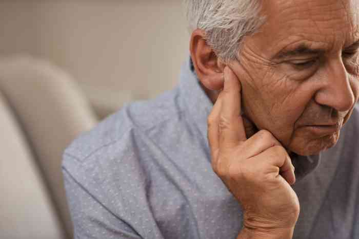 Senhor de idade com diminuição auditiva coloca os seus dedos no ouvido 