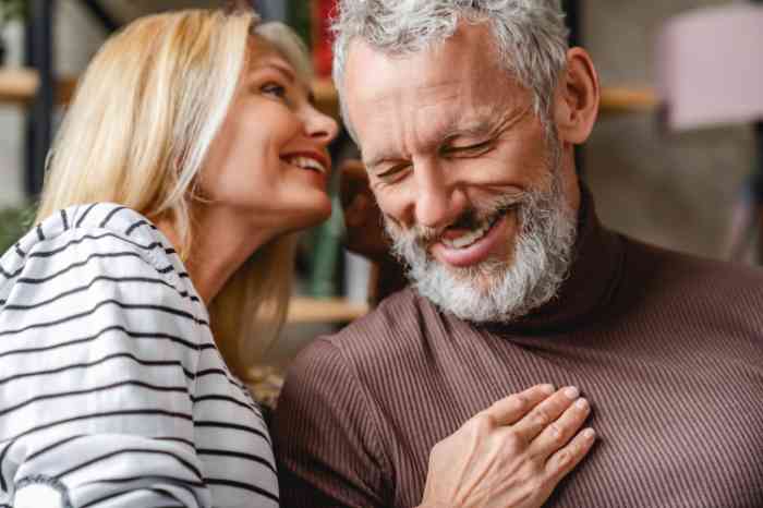 Casal de adultos alegres a sorrir com mulher a falar ao ouvido do homem.